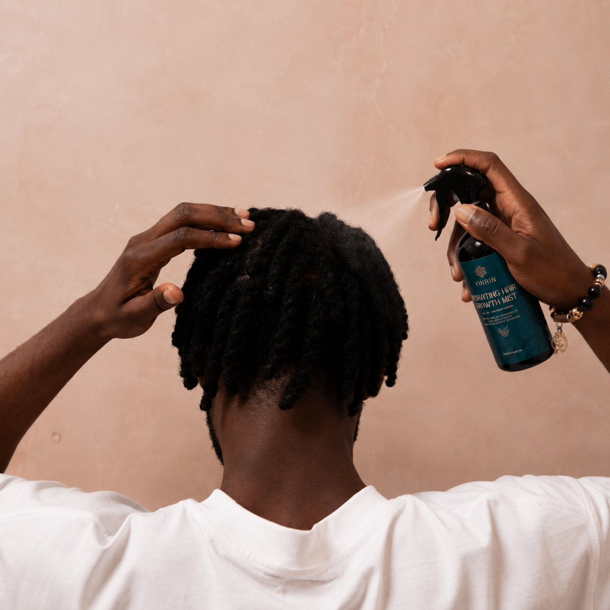 Person applying a product to their hair using a spray bottle against a beige background